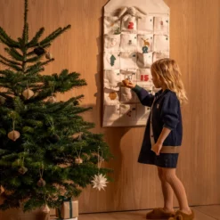 Kind steht vor dem aufgehängten Babbo-Adventskalender neben einem Weihnachtsbaum.
