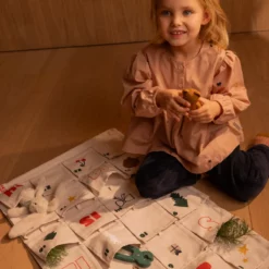 Kind sitzt auf einer gepolsterten Sitzfläche neben dem ausgebreiteten Babbo-Adventskalender.