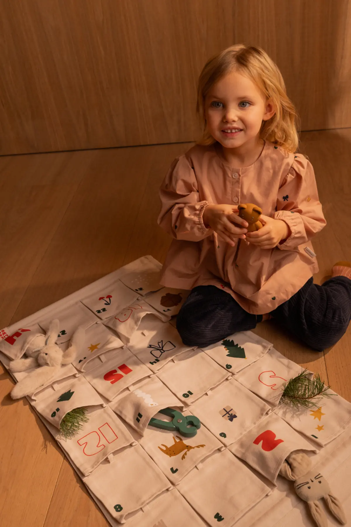 Kind sitzt auf einer gepolsterten Sitzfläche neben dem ausgebreiteten Babbo-Adventskalender.