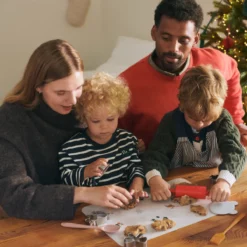 Kinder und ein Erwachsener bereiten gemeinsam Lebensmittel am Tisch vor; ein Kind trägt die Arda-Schürze.