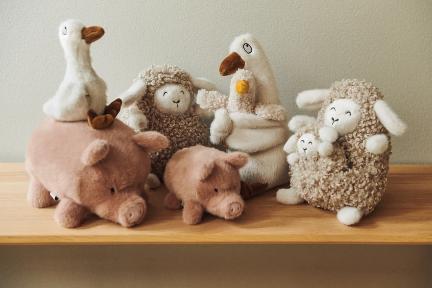 Schweinchen Spruce steht mit weiteren Liewood-Kuscheltieren auf einem Holzregal.